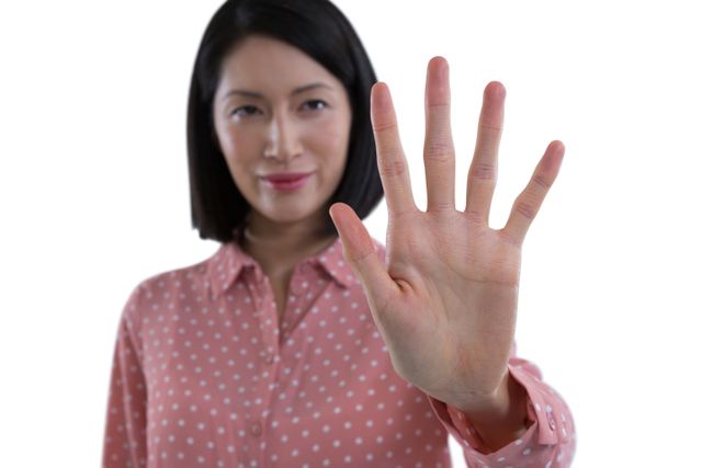 Woman in a pink polka dot shirt holding her hand up as if touching an invisible screen. Useful for illustrating concepts of technology, digital interfaces, and modern interaction. Ideal for use in tech blogs, digital marketing, and user interface design presentations.