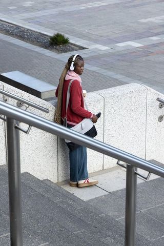 Young african american woman standing on urban stairs drinking coffee and using smartphone