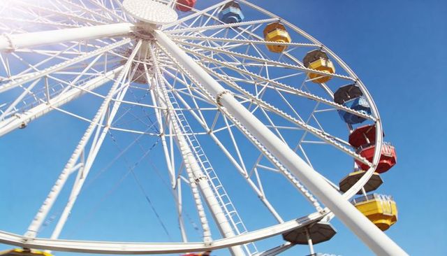 Soaring sunlit ferris wheel with colorful gondolas from low angle