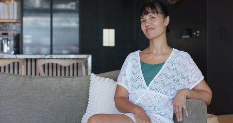 Mature woman sitting on sofa wearing lace coverup and teal camisole in contemporary lounge
