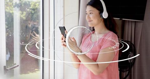 Asian woman wearing headphones using smartphone with futuristic hud overlay at home
