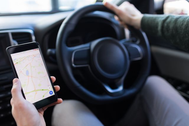 Cropped image of man holding smartphone with map while driving car