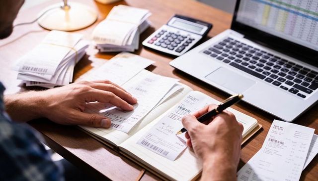 Small business owner tracking receipts and expenses at desk with laptop and calculator