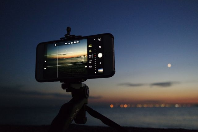 Capturing the calm evening sea with a smartphone on a tripod. Perfect for illustrations on mobile photography techniques, social media content creation, or tutorials on proper equipment use.