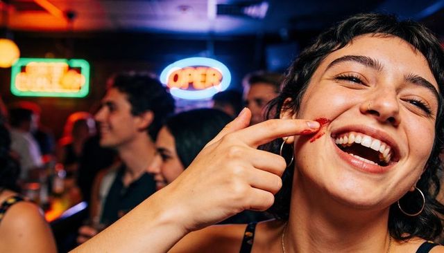 Young woman laughing and smearing red lipstick on cheek while partying in neon-lit bar