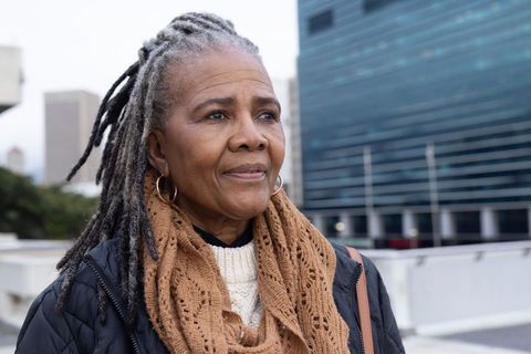 Senior african american woman gazing over urban skyline from rooftop wearing tan scarf