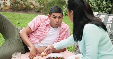 Young Couple Picnicking on Grass Sharing Snacks and Relaxing Outdoors