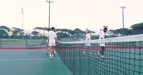 Multiracial male tennis players meeting and shaking hands at net on outdoor hard court