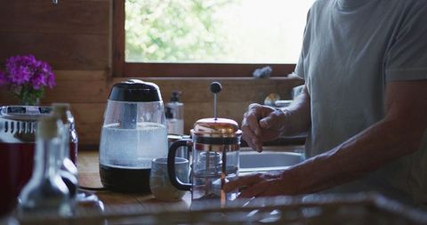 Senior man preparing french press coffee in sunlit kitchen