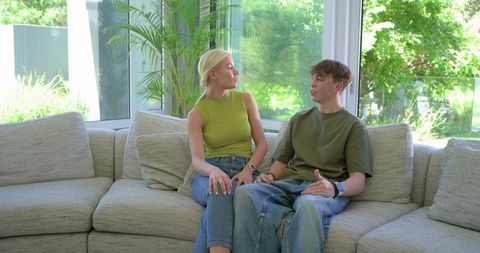Young woman and teenage boy sitting and talking on modern light-gray sectional sofa