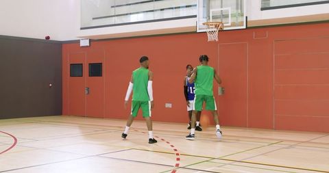 Black male basketball players executing quick pass and driving layup in indoor court