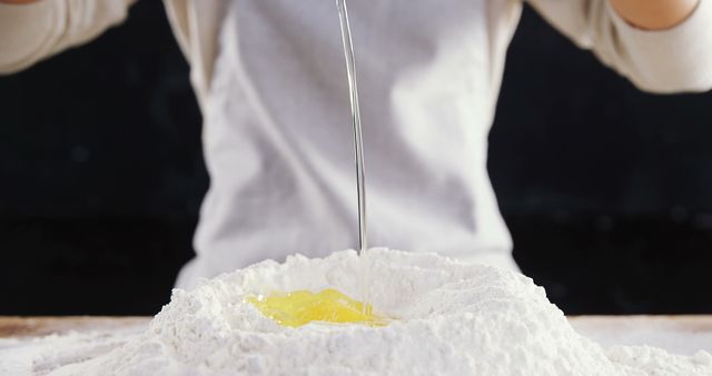 Person making dough with flour and egg in kitchen. Could be used for cooking blogs, recipes, culinary tutorials, or advertisements related to baking supplies and ingredients.