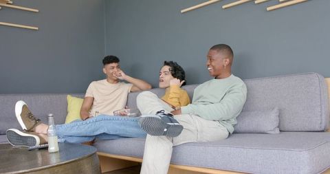 Diverse male friends lounging on modern gray sofa laughing and chatting in lounge