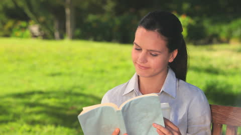 Woman Smiling While Reading at Park Bench