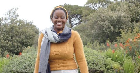 Smiling African American woman wearing mustard sweater and gray scarf in lush garden