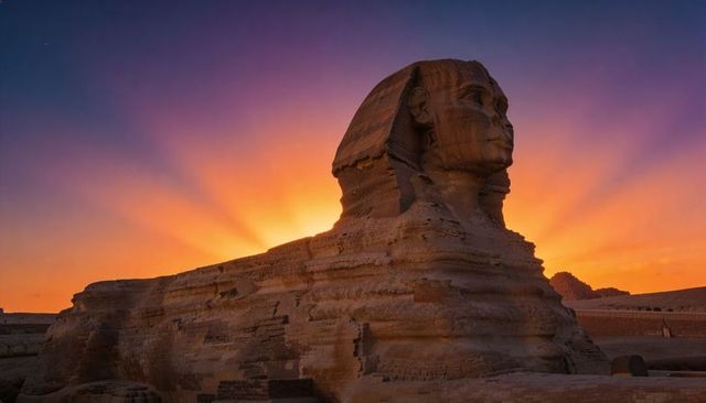 Great sphinx of giza glowing at dramatic sunset with radiant sky and weathered limestone
