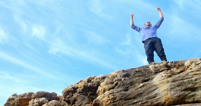 Man standing triumphantly on a rock with arms raised, celebrating victory. Use images for themes such as success, achievement, motivation, and outdoor adventure.