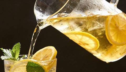 Pouring lemon iced tea from glass pitcher into mint-garnished tumbler