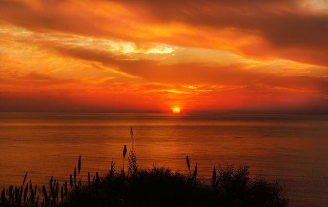 Capturing a peaceful sunset with vibrant orange hues across a calm ocean. The sky is adorned with clouds reflecting the rich colors of dusk, creating a serene and tranquil atmosphere. Perfect for backgrounds, nature themes, relaxation content, and travel promotions.