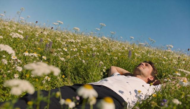 Man relaxing in wildflower meadow on sunny hill, lying and gazing at sky