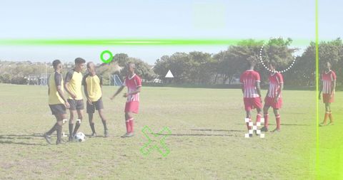 Standing around soccer ball, teammates discussing play on pitch with green graphic overlay