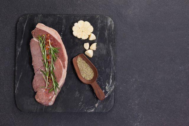Sirloin chop, garlic and spices on black slate plate against wooden background