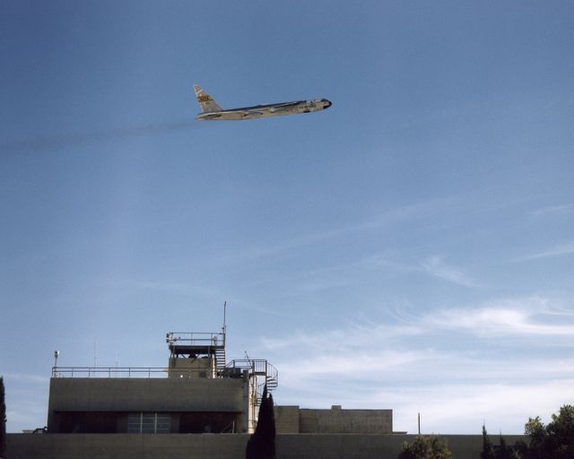 Image captures a high-altitude B-52 launch aircraft flying over a building at Dryden on a clear and sunny day. Suitable for websites and articles related to aerospace technology, military aviation, air force operations, and historical aviation achievements. The photo highlights the might of military aircraft and the expansive possibilities of aerial technology.