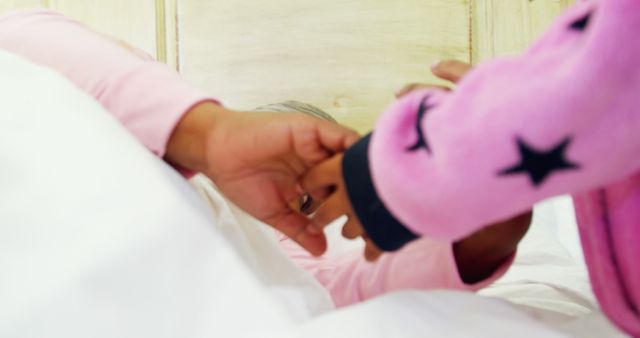 A young child in a pink outfit with star patterns is holding hands with an adult, with copy space. The image captures a tender moment of connection between a child and a parent or caregiver, evoking feelings of care and comfort.