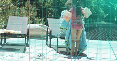 Adult wrapping child in towel on pool deck wearing hat and floaties, family pool safety