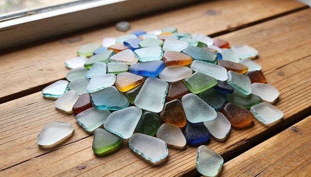 Sunlit sea glass pile on wooden sill catching daylight with cobalt aqua green brown tones