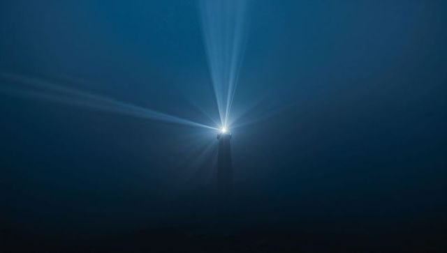 Solitary lighthouse piercing night fog with radiant beacon beams over dark ocean