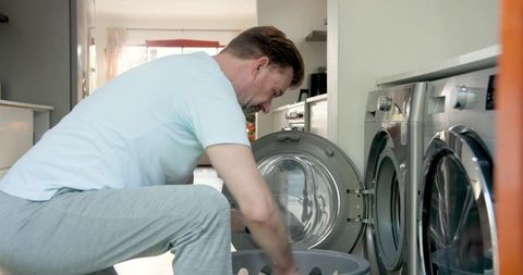 Mature man managing laundry loading washing machine in laundry room