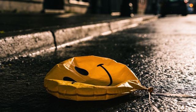 Deflated yellow smiley balloon resting on wet urban street at night with reflective puddles