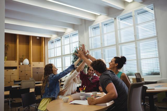 Young professionals celebrate success with a high five in a modern office. Ideal for depicting teamwork, collaboration, and corporate environment. Suitable for business promotions, office culture presentations, and motivational content.