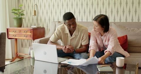 Interracial couple planning wedding using laptop in comfortable living room