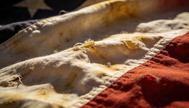 Weathered american flag close-up displaying frayed stripes and worn stitching