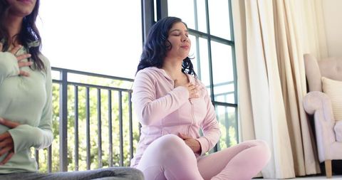 Diverse women practicing mindful breathing on home balcony in pink tracksuits