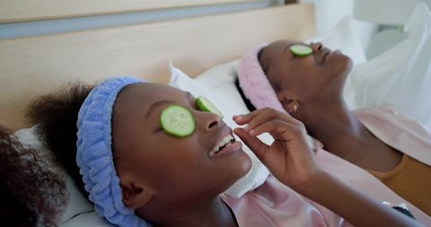 Mother and daughter enjoying at-home spa relaxing with cucumber eye slices and matching robes