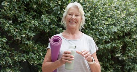 Senior woman smiling after outdoor yoga holding purple mat and water bottle wearing smartwatch