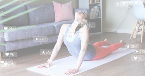Woman practicing backbend yoga at home mat while streaming workout with social media icons