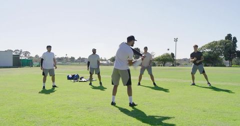 Summer baseball team practicing batting drill on sunny park field with yellow bat and gear