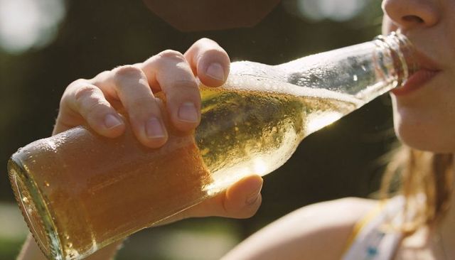 Sunlit woman sipping cold drink from glass bottle outdoors closeup summer refreshment