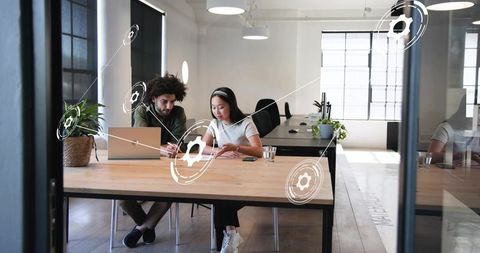 Collaborating colleagues discussing data on laptop in bright modern open-plan office