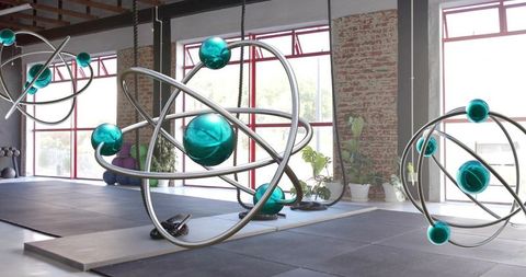 Hanging orbital sculptures with teal glass spheres in industrial loft studio with rope suspension