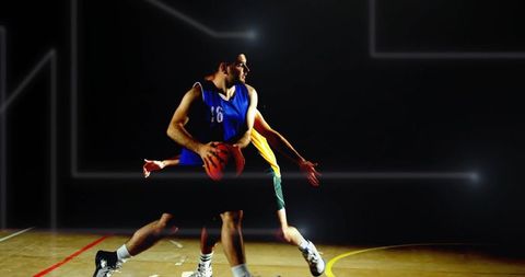 Basketball player shielding ball while driving past defender under spotlight on hardwood court