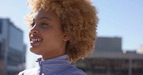 Sunlit urban woman smiling on rooftop in light purple active jacket promoting fitness
