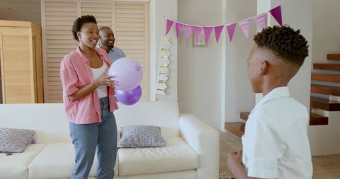 African American Family Celebrating Birthday at Home Holding Purple Balloons and Banner