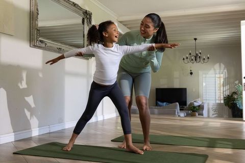 Asian mother guiding african american daughter practicing balance yoga at home on mats
