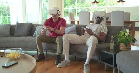 Diverse friends playing multiplayer VR games on sofa, relaxed modern living room vibe