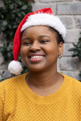 Smiling african american woman wearing santa hat and mustard sweater in festive courtyard